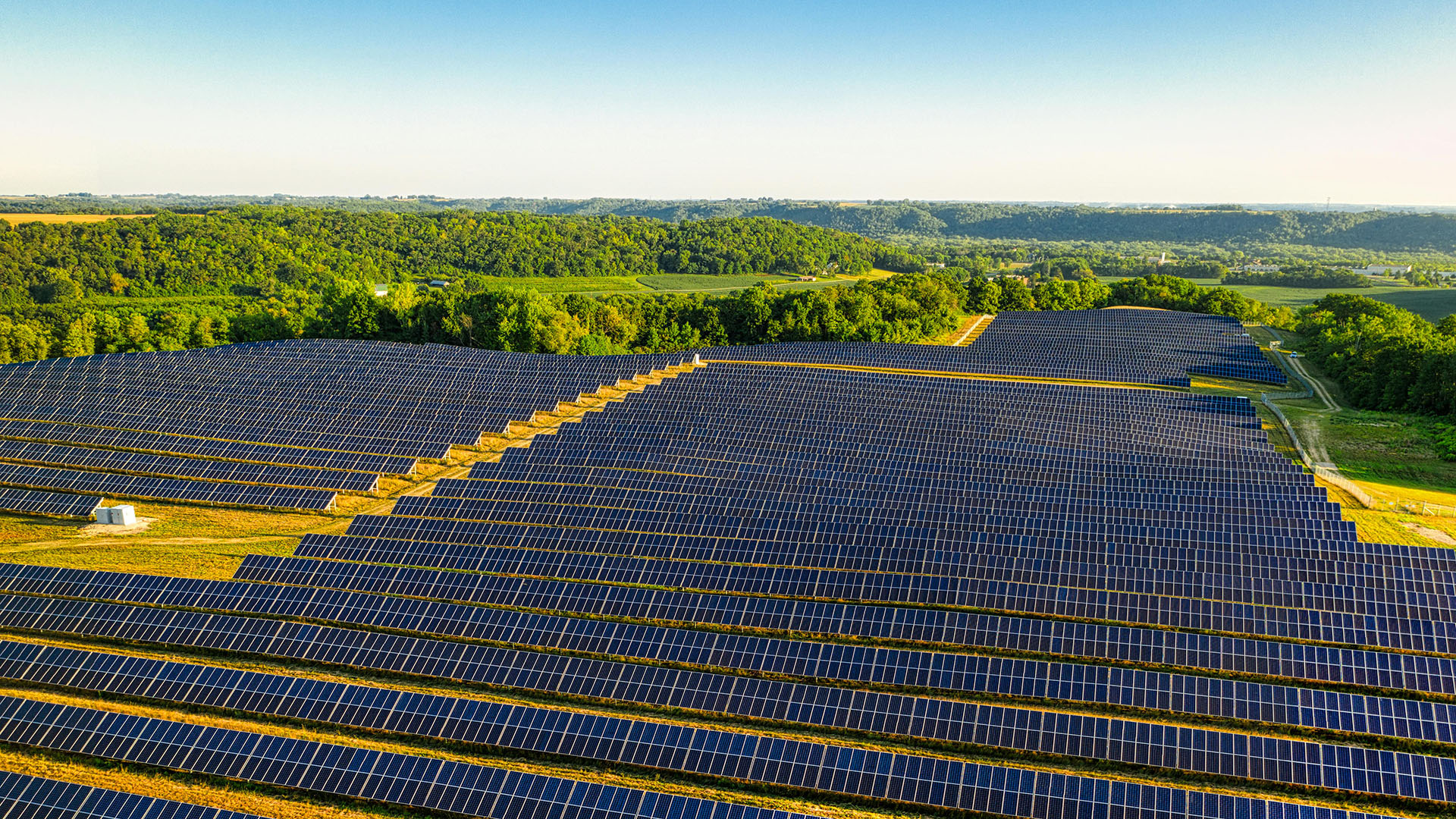 Drone-eye view of a large solar farm with green forest in the distance