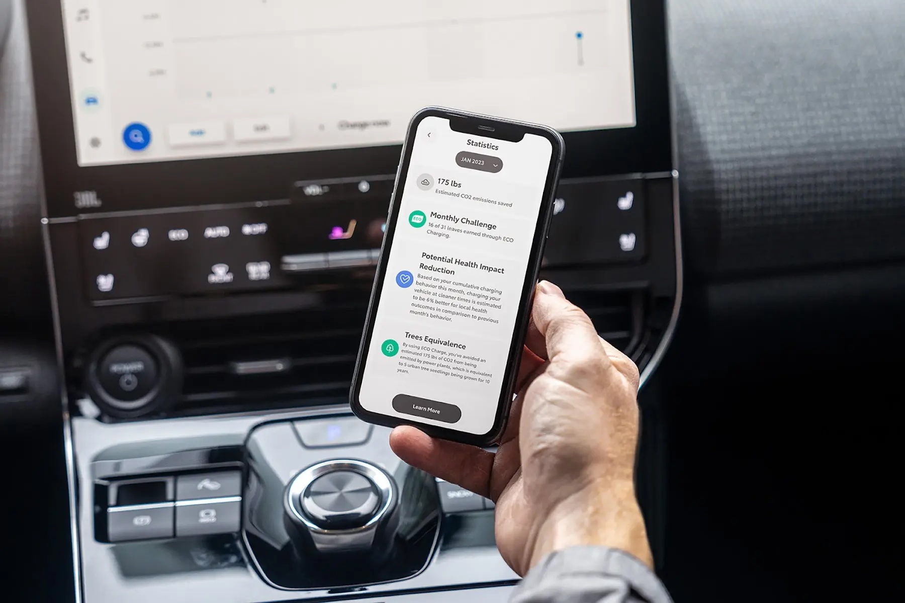 Cell phone held in a hand in a car with emission reduction information on the screen