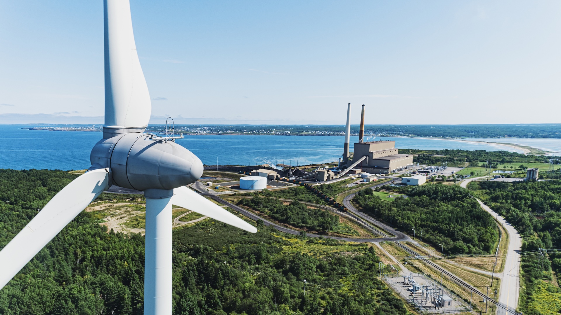 Aerial drone view of a wind turbine in the foreground of a coal fired power generating station.